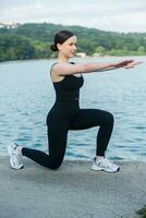 Jeune femme dans noir tenue de sport exercice en plein air. aptitude et en bonne santé mode de vie concept. le blanc fille Est-ce que des sports dans le parc. photo