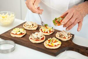 ajouter garnitures à le mini pizzas. ajouter des légumes. délicieux fait maison mini pizzas préparation. photo