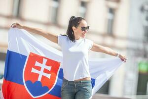 magnifique Jeune femme détient une drapeau de la slovaquie à l'extérieur sur une ensoleillé jour, portant des lunettes de soleil photo