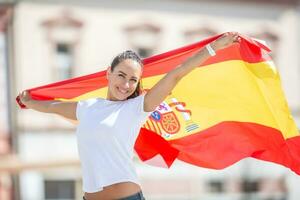 content souriant jolie fille détient une drapeau de Espagne derrière sa célébrer sur une rue photo