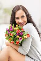 content foncé aux cheveux femme en portant une charmant bouquet plein de tulipes pendant nationale aux femmes journée photo
