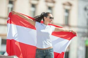 jolie fille dans des lunettes de soleil et bras large ouvert détient autrichien drapeau sur une rue photo