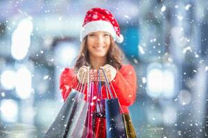 Noël achats. attrayant content fille avec crédit carte et achats Sacs dans Père Noël chapeau. neigeux atmosphère. photo