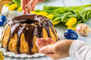 délicieux vacances slovaque et tchèque gâteau babovka avec Chocolat glaçage. femelle mains décorer une gâteau .Pâques décorations - printemps tulipes et des œufs photo