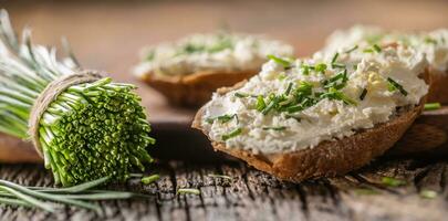 ciboulette crème fromage propager sur une pain tranches suivant à bouquet de fraîchement Couper ciboulette sur une rustique bois et couper planche photo