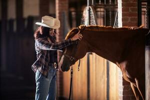 Jeune cow-girl prend bride de le les chevaux tête à l'intérieur le stable après une conduire. photo