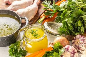 poulet bouillon dans une verre pot brut poulet jambes carotte oignon céleri herbes Ail et Frais des légumes photo