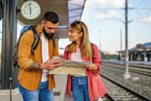 couple est permanent à chemin de fer station et attendre pour arrivée de leur train. elles ou ils sont à la recherche à carte. photo