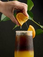 glacé café avec Orange jus dans une transparent verre, une femme main serre un Orange tranche dans une bulle boisson photo