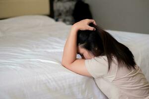 triste déprimé Asie femme Souffrance sur le blanc lit, elle est séance dans lit et émouvant sa front, sommeil désordre et stress concept photo