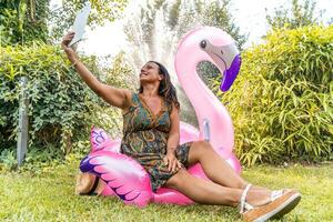 magnifique souriant milieu vieilli femme prise une selfie séance sur une rose flamant gonflable jouet photo