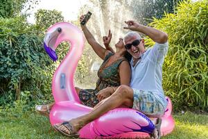 magnifique souriant milieu vieilli couple prise une selfie séance sur flamant gonflable jouet photo