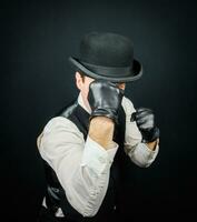 portrait de dangereux ancien combattant dans gilet et melon chapeau permanent dans karaté position. gangster dans noir cuir gants. photo