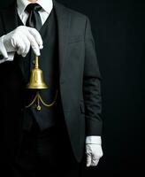 portrait de majordome ou Hôtel la conciergerie dans foncé costume et blanc gants en portant une or cloche. bague pour un service concept. photo