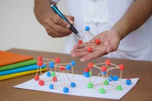 proche en haut prof mains tenir stylo et scientifique modèle enseignement aide à enseigner à propos moléculaire structures, fabriqué de pâte à modeler des balles avec dent choix des bâtons. concept, science éducation. photo