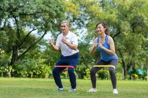 Sénior asiatique homme et le sien fille sont en utilisant sport caoutchouc bande à construire en haut le sien jambe muscle force dans le Publique parc pour aîné longévité exercice et Extérieur faire des exercices photo