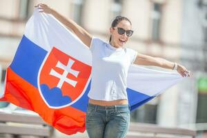 magnifique Jeune femme détient une drapeau de la slovaquie à l'extérieur sur une ensoleillé jour, portant des lunettes de soleil photo