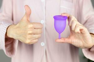 fermer de une femme mains en portant une silicone menstruel Coupe. alternative écologique féminin hygiène produit pendant menstruation sans déchets concept photo