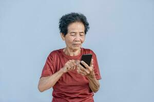 asiatique Sénior femme sourit et vidéo appel isolé dans gris Contexte. fort personnes âgées grand-mère sentiment content en utilisant mobile cellule téléphone à communiquer avec famille et prendre plaisir retraite la vie dans maison. photo