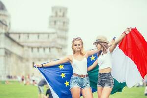 Jeune adolescent les filles voyageur avec italien et européen syndicat drapeaux avant le historique la tour dans ville pise - Italie photo