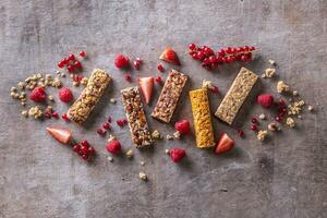 divers muesli bars avec groseilles, framboises et des fraises comme bien comme céréales autour eux, vu de le Haut photo