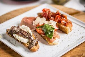 savoureux italien apéritif bruschette avec tomates anchois prosciutto et Mozarella photo