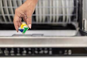 détail de une femelle main en mettant coloré détergent tablette dans le Lave-vaisselle photo