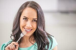une magnifique Jeune femme avec une fourchette dans sa bouche est en pensant avec le tentation à manger photo