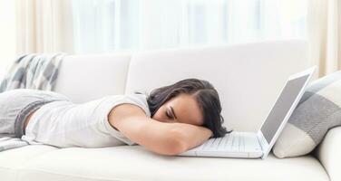 fatigué femme qui est tombée endormi sur sa portable mensonge sur une canapé dans une blanc environnement de une vivant pièce photo