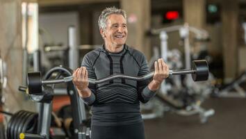 homme dans gris cheveux tirant poids à l'intérieur le Gym photo