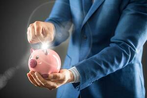 économie argent. homme d'affaires en portant rose porcin et en mettant pièce de monnaie dans porcin banque. photo