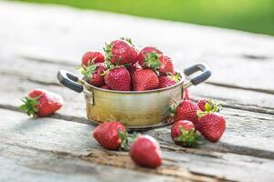 Frais mûr des fraises dans ancien cuisine pot sur vieux jardin table photo