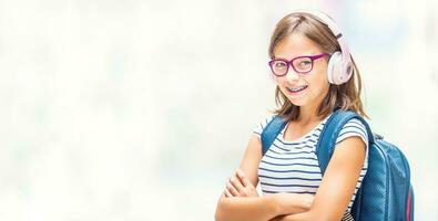portrait de moderne content adolescent école fille avec dentaire un appareil dentaire des lunettes sac sac à dos et écouteurs photo