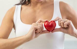 femme détient petit rouge cœur plus de sa poitrine dans le zone où le réel cœur est comme une symbole de cœur maladies la prévention photo