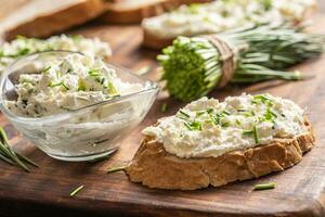 une bol de fait maison crème fromage propager avec haché ciboulette entouré par pain tranches avec propager et une bouquet de fraîchement Couper ciboulette photo