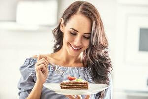 en couches marron adn blanc gâteau avec fraise et menthe feuille sur Haut tenue par une femme avec une fourchette photo