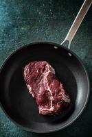 Haut vue de une foncé la poêle avec une brut tronçon de steak Viande sur une marbre surface photo