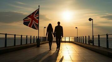 couple en marchant en dessous de Britanique drapeau sur côtier promenade dans Angleterre à le coucher du soleil. silhouette concept photo