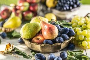 mûr des fruits sur le table dans le jardin. Frais poires dans une bronze bol entouré par une variété de jardin des fruits photo