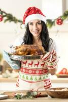 satisfait Jeune femme dans une Noël tablier et Père Noël chapeau en portant une grillage la poêle avec une rôti OIE ou dinde photo