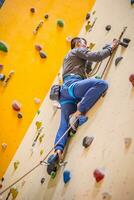 grimpeur sur mur.jeune homme pratiquant Roche escalade sur une Roche mur à l'intérieur photo