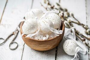 Fait main blanc Pâques des œufs avec saule chatons dans une en bois bol sur en bois table photo