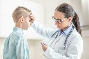 médecin femme est mesure le Température de Jeune garçon dans médical Bureau photo