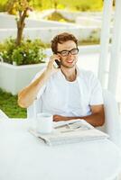 une homme dans des lunettes en train de lire une journal tandis que séance à une table photo