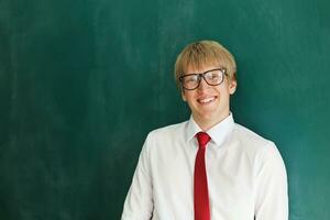 une Jeune homme dans des lunettes et une attacher permanent dans de face de une tableau noir photo