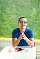 une homme dans des lunettes séance à une table avec une tasse de café photo