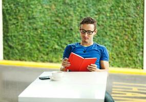 une homme dans des lunettes séance à une table avec une tasse de café photo