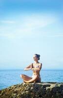 une femme dans une yoga pose sur une Roche par le océan photo