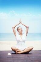 une femme dans blanc est Faire yoga sur le plage photo