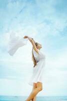 une femme dans une blanc robe permanent sur le plage avec une blanc tissu photo